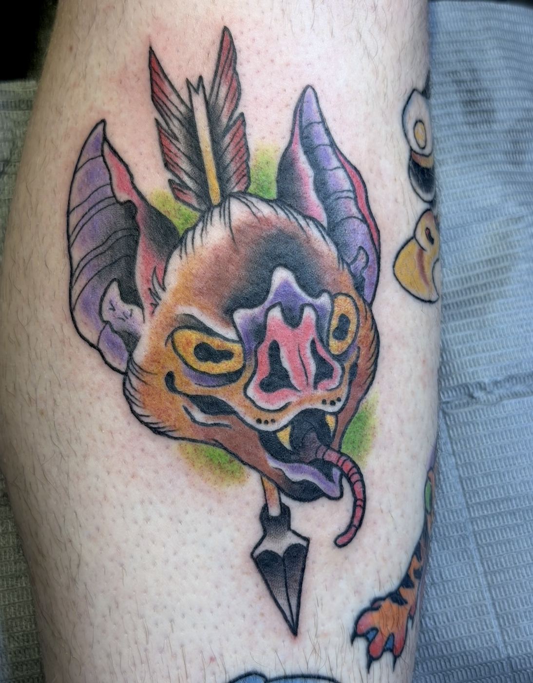 Purple and pink bat head tattoo pierced by an arrow