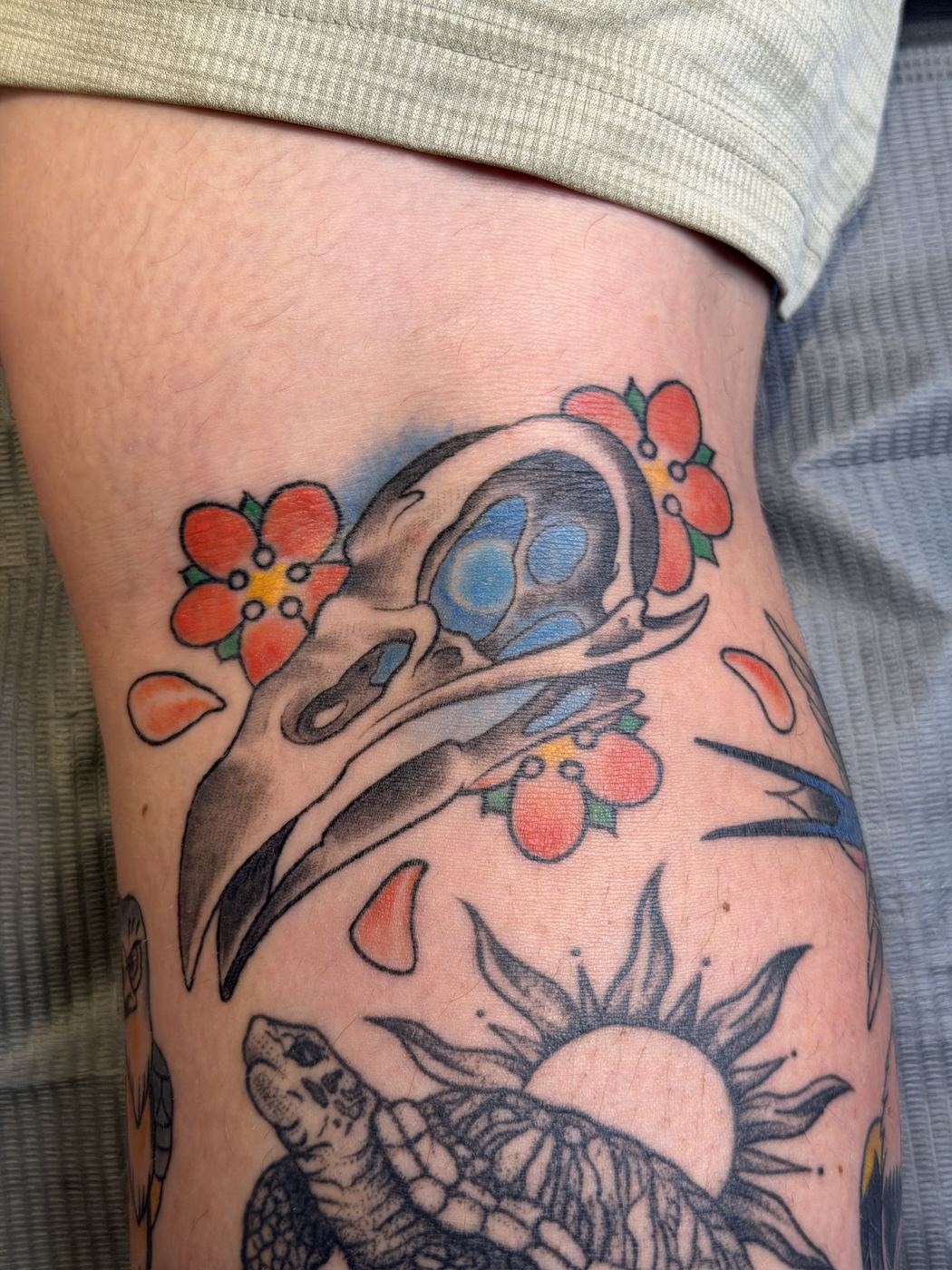 Bird skull tattoo with blue eye sockets framed by red flowers
