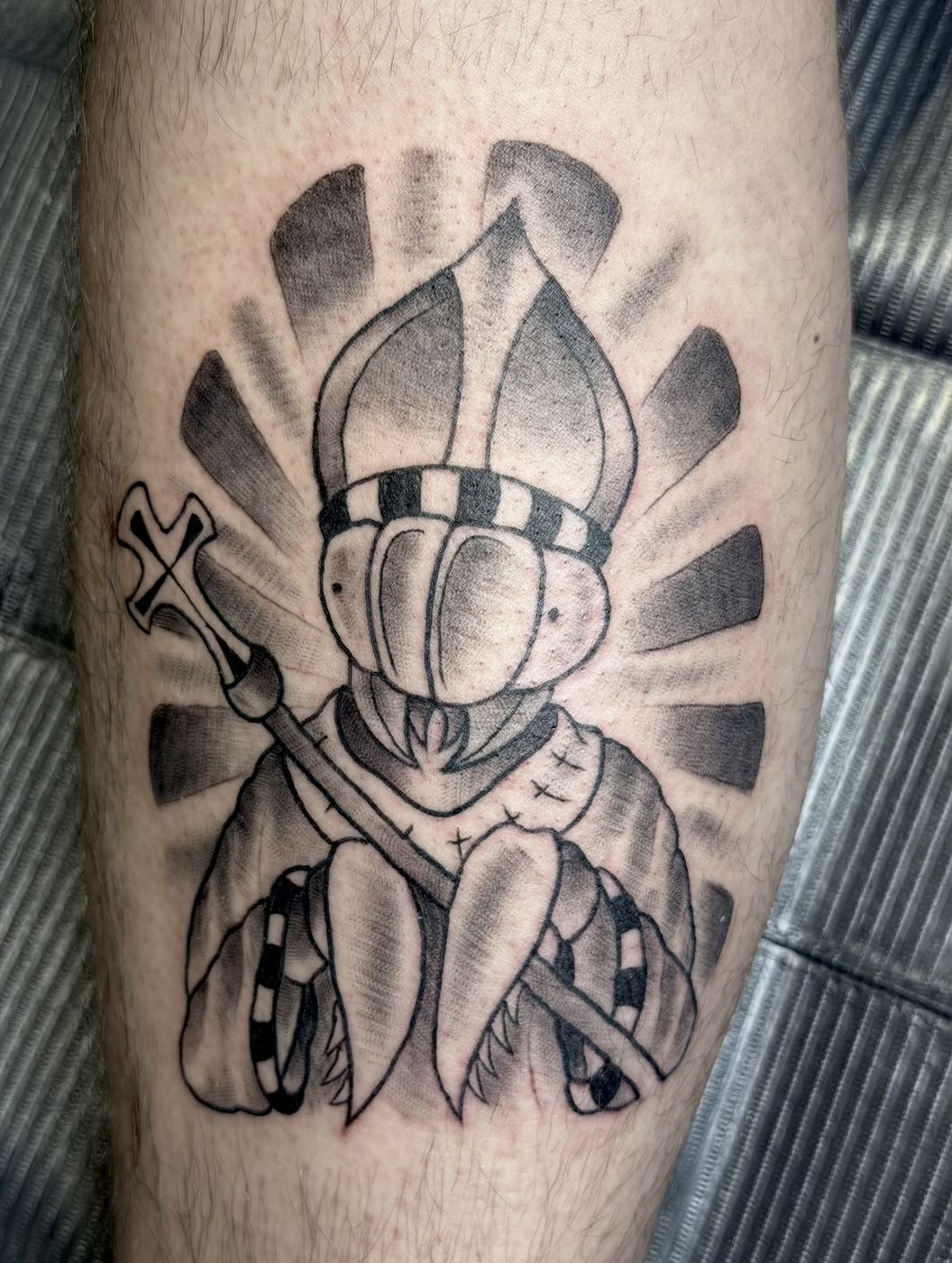 Black and grey bishop tattoo holding a crozier with a radiating sunburst background