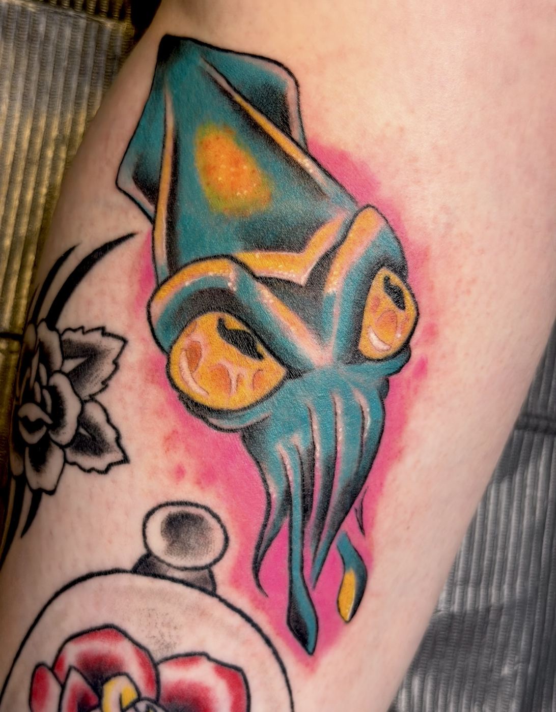 Teal and orange ghost-like creature tattoo on a pink background