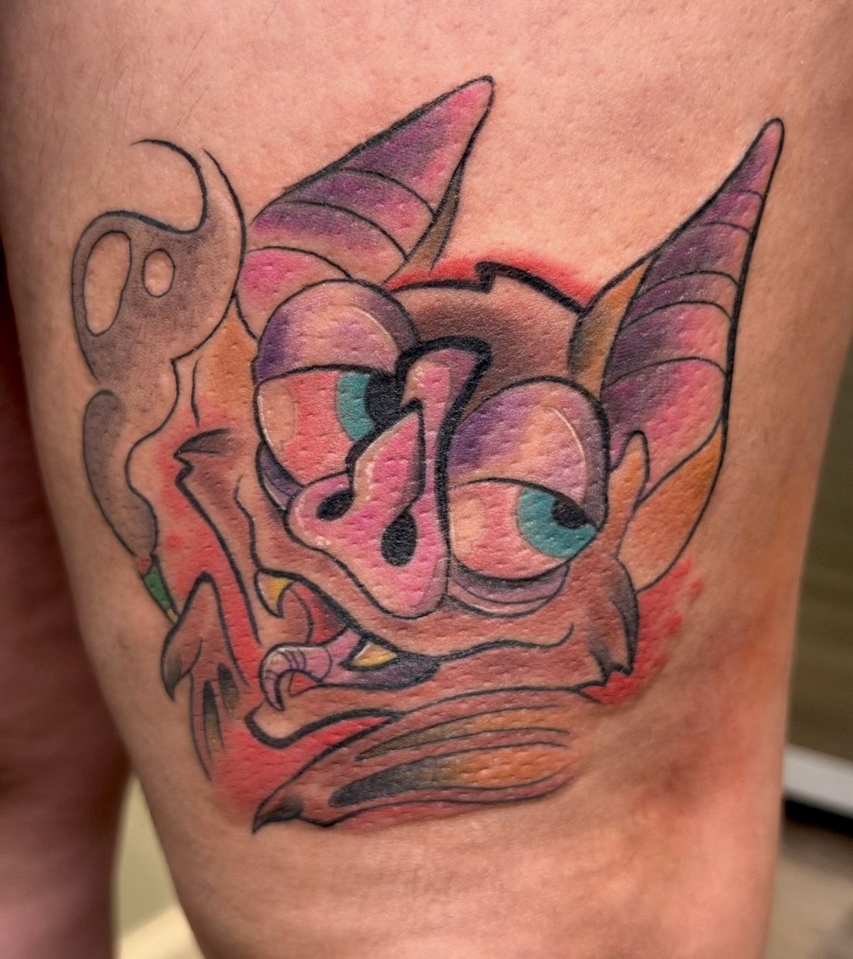 Pink and purple gremlin face tattoo with large eyes