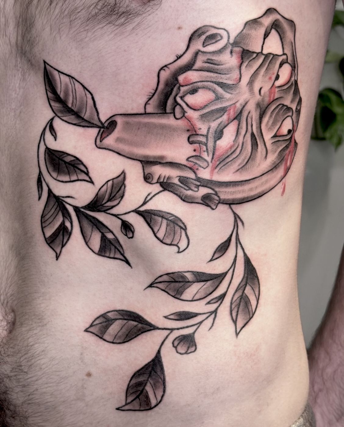 Black and grey hand holding a bleeding heart tattoo with a leafy vine