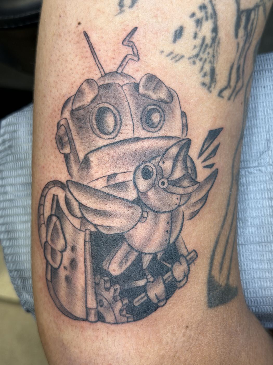 Black and grey mechanical bird bursting from a robot head tattoo