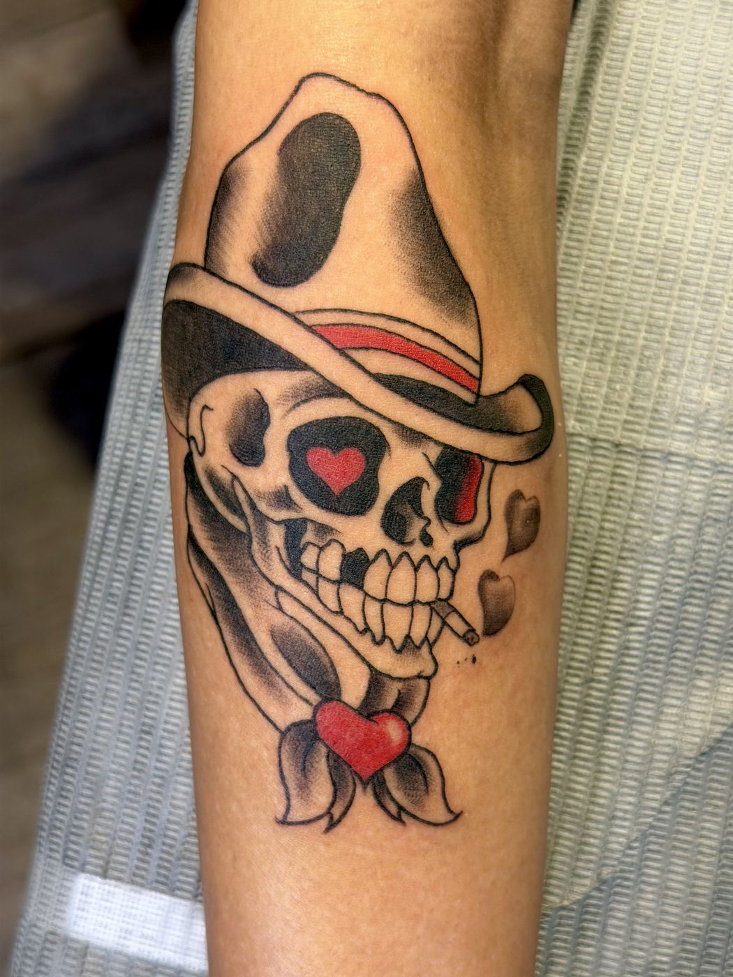 Skull tattoo wearing a cowboy hat with hearts and a lit cigarette