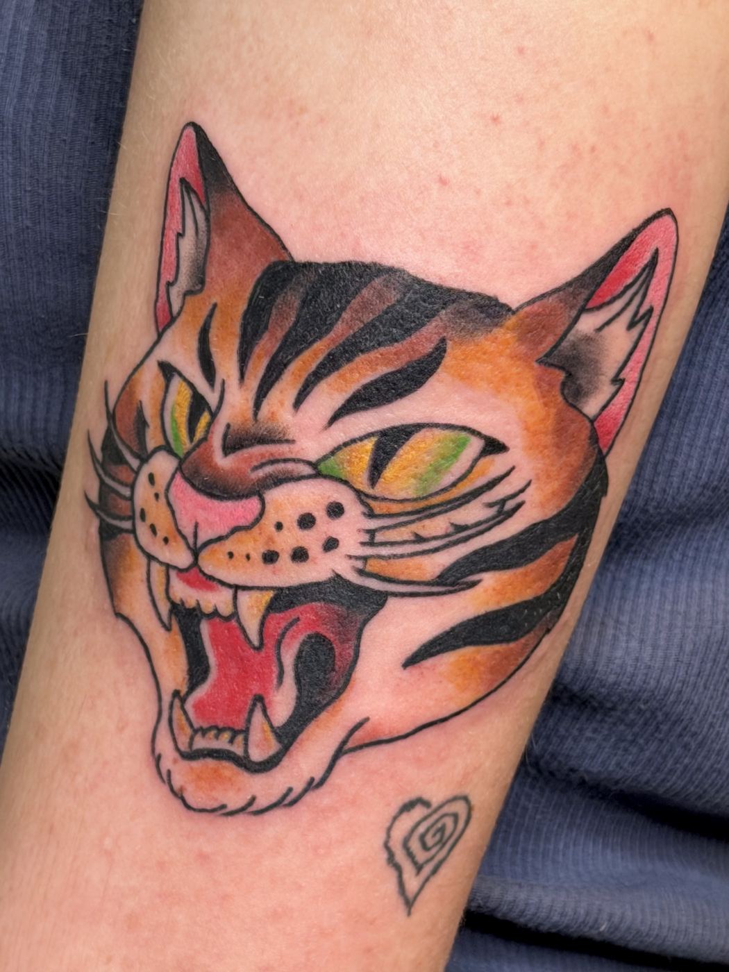 Color tattoo of a roaring tabby cat head with pink ears and green eyes